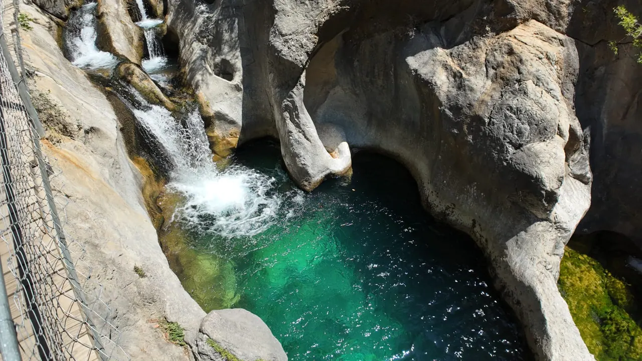 Une cascade écumante tombant dans un bassin vert émeraude profond, sous un surplomb calcaire du canyon de Sapadere