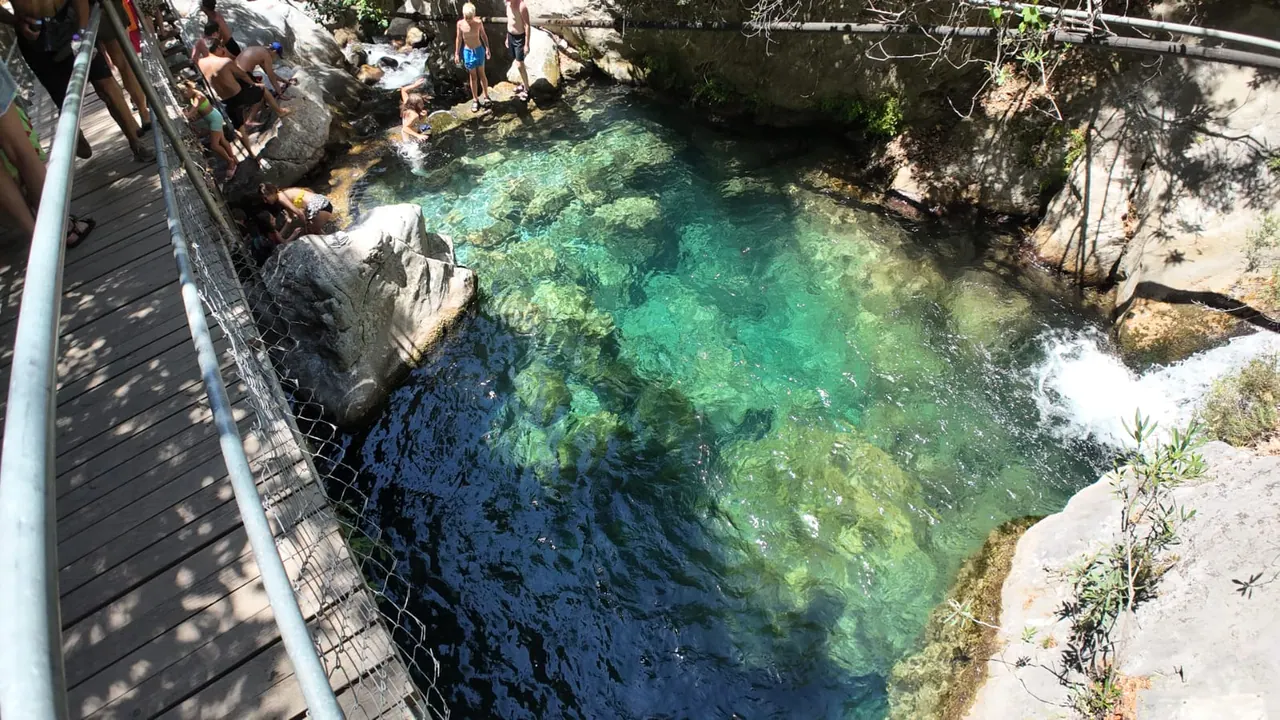 Holzsteg mit Metallhandlauf entlang eines klaren grünen Beckens im Sapadere Canyon