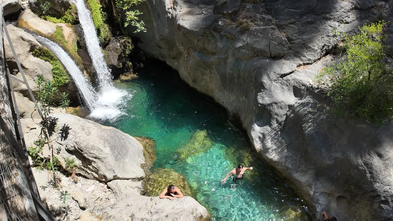 Zwei Wasserfälle, die in ein tiefes smaragdgrünes Becken der Schlucht stürzen, mit Schwimmern im klaren Flachwasser